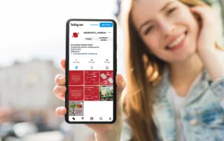 Eine junge Frau mit Jeansjacke zeigt ihr Handy in die Kamera. Auf diesem sieht man das Instagram-Profil der Satztechnik Meißen